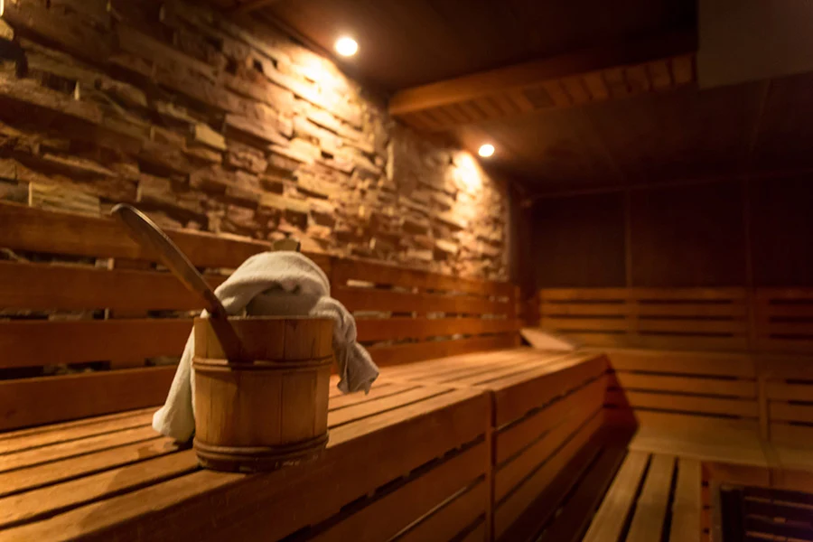Finnish sauna with wooden benches, water bucket and natural stone wall at Lokahi Loft Berlin